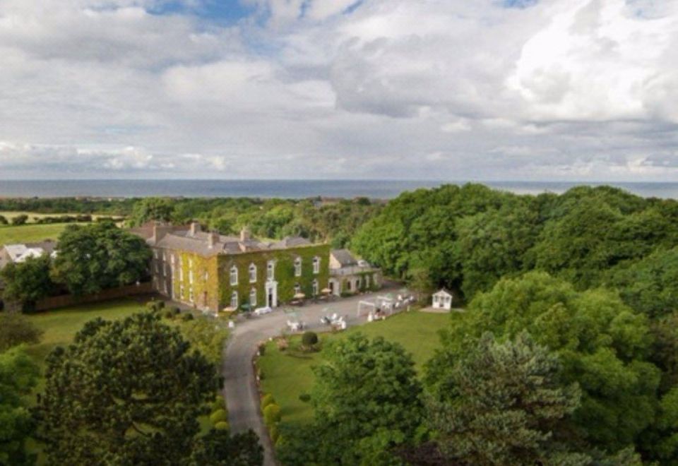 aerial view of a large , yellow building surrounded by trees and a body of water at Hardwicke Hall Manor Hotel