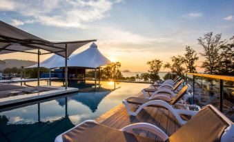 a serene poolside setting with several lounge chairs and umbrellas , set against the backdrop of a beautiful sunset at Beyond Patong