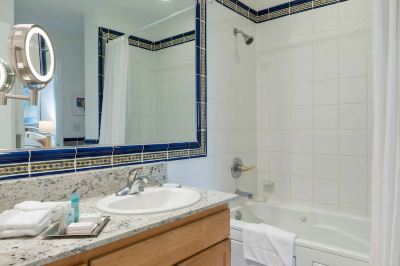 a bathroom with a white bathtub , sink , and mirror , as well as a wooden cabinet at Wyndham Reef Resort Grand Cayman