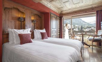 a woman in a white dress standing in a bedroom with two beds , one on each side of the room at Hotel Mont Blanc Megève
