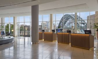 a modern hotel lobby with a check - in desk , large windows , and a view of the ocean at Hilton Newcastle Gateshead