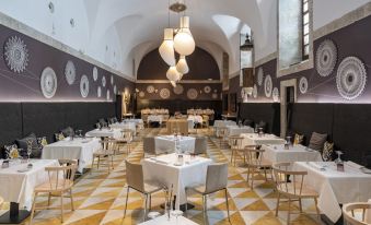 a large , empty dining room with multiple tables and chairs , a checkered floor , and multiple hanging lights at Parador Monasterio de Corias