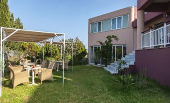 a large house surrounded by a lush green lawn , with a dining table and chairs set up for a meal at Sofi