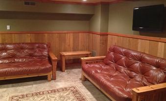 a cozy living room with two red leather couches and a wooden coffee table , surrounded by wooden walls and a rug on the floor at Cranberry Inn