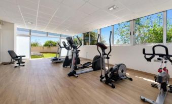 a well - equipped gym with various exercise equipment , including treadmills and stationary bikes , near large windows that offer views of the outdoors at Hotel Areca