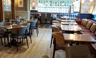 a modern cafe with wooden floors , large windows , and various seating arrangements , including stools and tables at Premier Inn Wirral (Greasby)