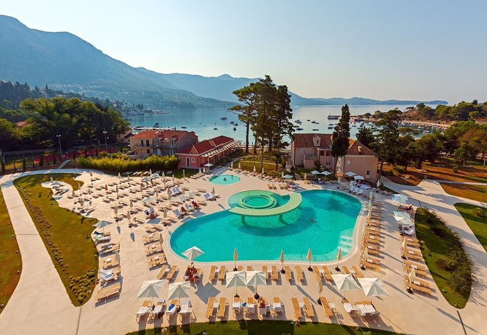 a large outdoor swimming pool surrounded by lounge chairs and umbrellas , with a view of the ocean in the background at Sheraton Dubrovnik Riviera Hotel