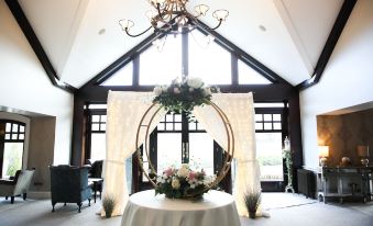 a round table with a centerpiece of flowers and roses is set up in front of a large window at Mulroy Woods Hotel