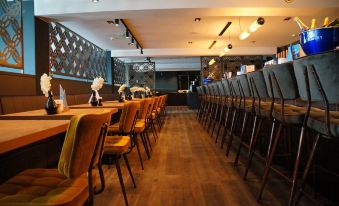 a restaurant with wooden tables and chairs , some of which are empty , and a bar area in the background at Fletcher Hotel Restaurant Loosdrecht-Amsterdam