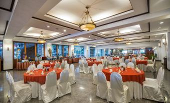 a large banquet hall with multiple dining tables and chairs , some of which are covered in white tablecloths at Royal Tretes View Hotel & Convention