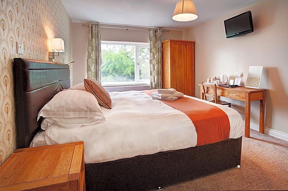 a large bed with a white and orange blanket is in a room with a wooden nightstand at The Twice Brewed Inn