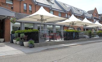 an outdoor dining area with several umbrellas providing shade for people sitting at tables and enjoying their meals at Glynhill Hotel & Spa Near Glasgow Airport