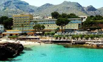 a beautiful beachfront hotel with a large hotel building and swimming pool , surrounded by clear blue water and mountains in the background at Grupotel Molins