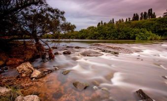 a river flowing through a rocky landscape with trees and bushes on the banks , under a cloudy sky at Discovery Parks - Hadspen