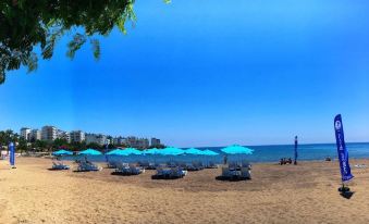 a beach scene with several blue umbrellas and lounge chairs scattered around the sand , creating a relaxing atmosphere at Palm Beach Hotel