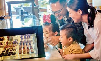 A woman and a young girl are looking at food in a window while another person stands next to them at Disney Explorers Lodge