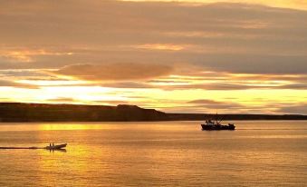 a sunset over a calm body of water with a boat in the distance and clouds overhead at The Florian Hotel