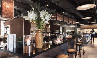 a modern bar with a vase of white flowers on the counter , surrounded by chairs and bottles at Quality Hotel Winn Haninge