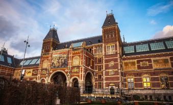 a large , ornate building with a red and gold facade is surrounded by greenery and has two tall towers on either side at Best Western Plus Hotel Amstelveen