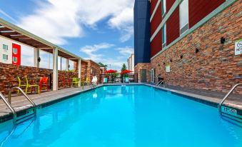 an outdoor swimming pool surrounded by a brick building , with several umbrellas placed around the pool area at Home2 Suites by Hilton Gonzales