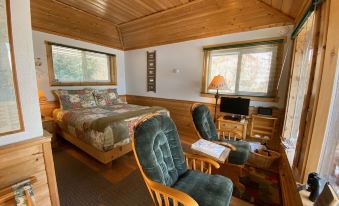 a cozy bedroom with a wooden bed , two green armchairs , and a television , all set against a backdrop of wood paneling at Angels Rest on Resurrection Bay LLC