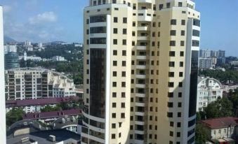 a tall , white building with black windows and balconies stands against a blue sky , overlooking other buildings in the background at Luxury Apartment