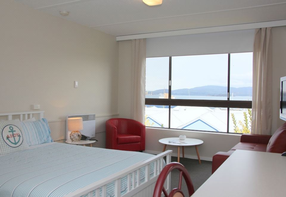 a hotel room with a bed , a chair , and a window overlooking the ocean at Beauty Point Waterfront Hotel