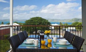 a table with plates , cups , and a pitcher of orange juice is set on a balcony overlooking the ocean at Island Villas