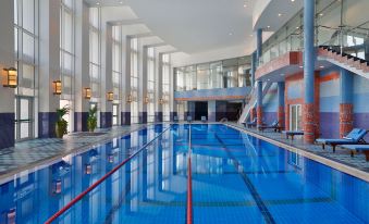 an indoor swimming pool with a blue tiled floor , surrounded by glass walls and overlooking a building at The Ritz-Carlton, Doha