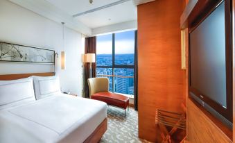 The bedroom features large windows and a balcony that overlook the city, with an unmade bed at Swissotel Foshan Guangdong