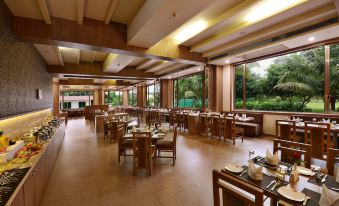 a large , well - lit dining room with multiple tables and chairs arranged for a group of people at Sarovar Portico Sasangir