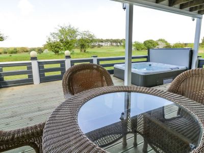 a patio with a hot tub and a table , surrounded by wicker chairs and a view of a golf course at Moon Face