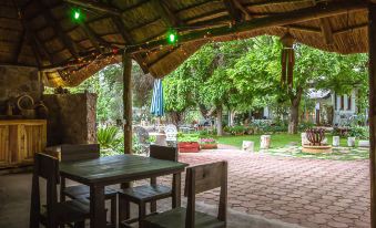 a wooden table and chairs are set up under a thatched roof in a garden at Morning Glory Cottages