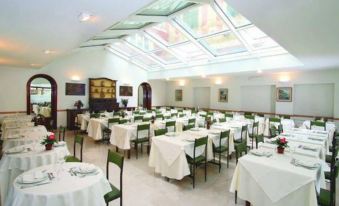 a large , empty dining room with white tables and chairs , surrounded by windows that allow natural light to enter at Hotel Le Palme