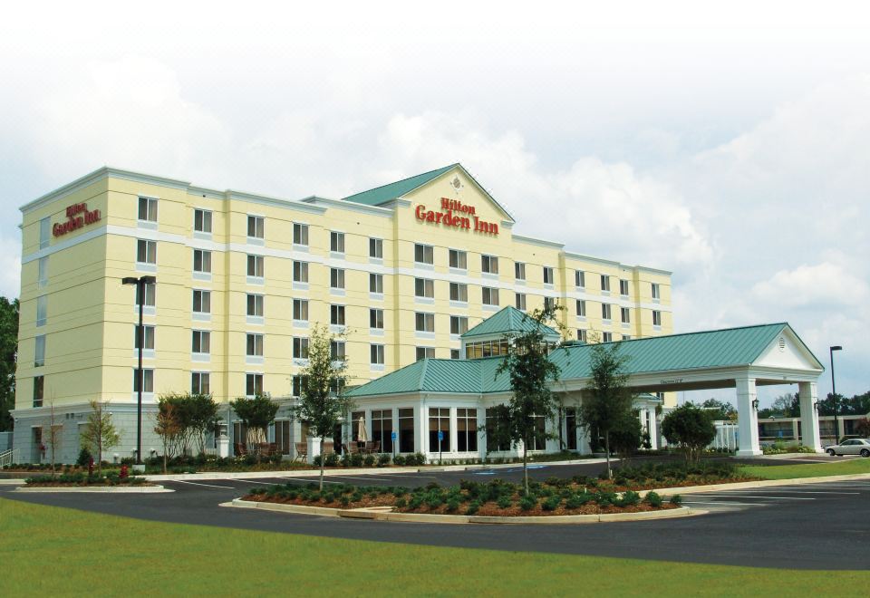a large hotel building with multiple floors , surrounded by trees and grass , under a cloudy sky at Hilton Garden Inn Meridian