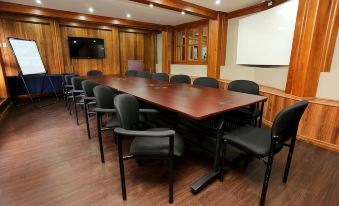 a conference room with a long wooden table , black chairs , and a large screen on the wall at Tradewinds Hotel