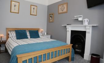 a cozy bedroom with a blue bedspread , wooden bed frame , and white walls , along with a fireplace and television at Acorns Guest House