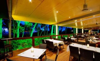an indoor dining area with wooden floors , tables , chairs , and a large projection screen on the wall at Albatross Bay Resort