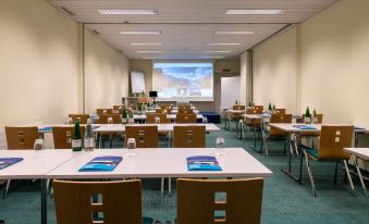 a large conference room with multiple tables and chairs , a projector screen , and bottles of water on the tables at Arenas Resort Victoria-Lauberhorn