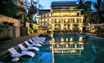 a large swimming pool with white lounge chairs is in front of a building at dusk at Le Meridien Goa, Calangute