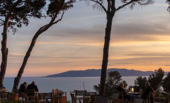 a serene sunset view of a beach and mountains , with people sitting at a table and tables outside at Boutique Hotel Torre di Cala Piccola