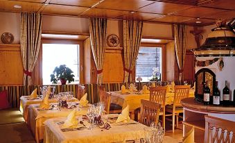 a well - decorated restaurant with wooden furniture , large windows , and multiple tables set for dining , along with wine glasses and bottles at Hotel Goldener Adler