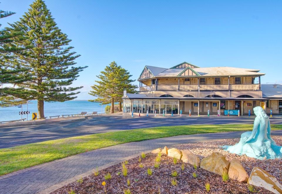 a building with a large window and balcony is situated next to a beach , surrounded by trees and bushes at Aurora Ozone Hotel Kangaroo Island