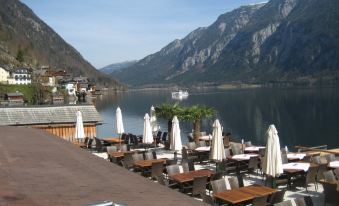 a serene mountainous landscape with a calm lake , and several tables and chairs set up for outdoor dining near the water at Seehotel Gruner Baum