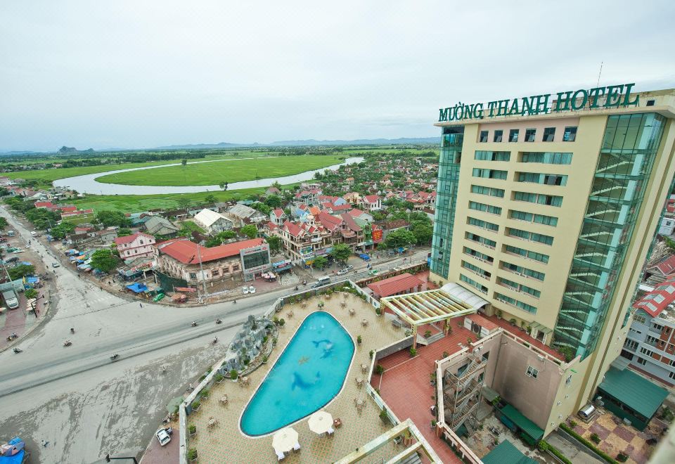 a large hotel with a pool surrounded by grass , trees , and buildings in the background at Muong Thanh Dien Chau Hotel