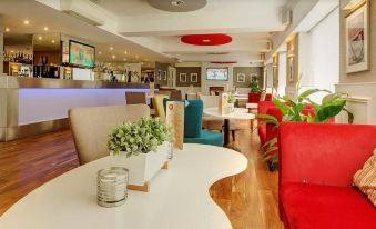a modern restaurant with a bar and dining area , featuring white tables and red chairs at The Park Hotel