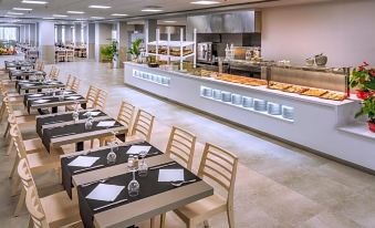 a large dining area with several tables and chairs , a buffet in the background , and a few potted plants on the tables at Hotel Sorra Daurada Splash