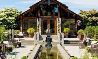 a modern wooden house with a large window and glass door , surrounded by lush greenery and flowers , and a water feature in front of it at The Inn at Langley