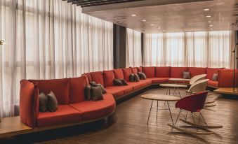 a large red couch is in a room with white walls and wooden floors , and several chairs at Ibis Carlos Barbosa