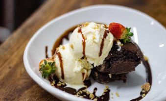 a white plate with a scoop of chocolate ice cream topped with strawberries , drizzled with chocolate sauce and drizzled with nuts at Hacienda Los Molinos Boutique Hotel & Villas